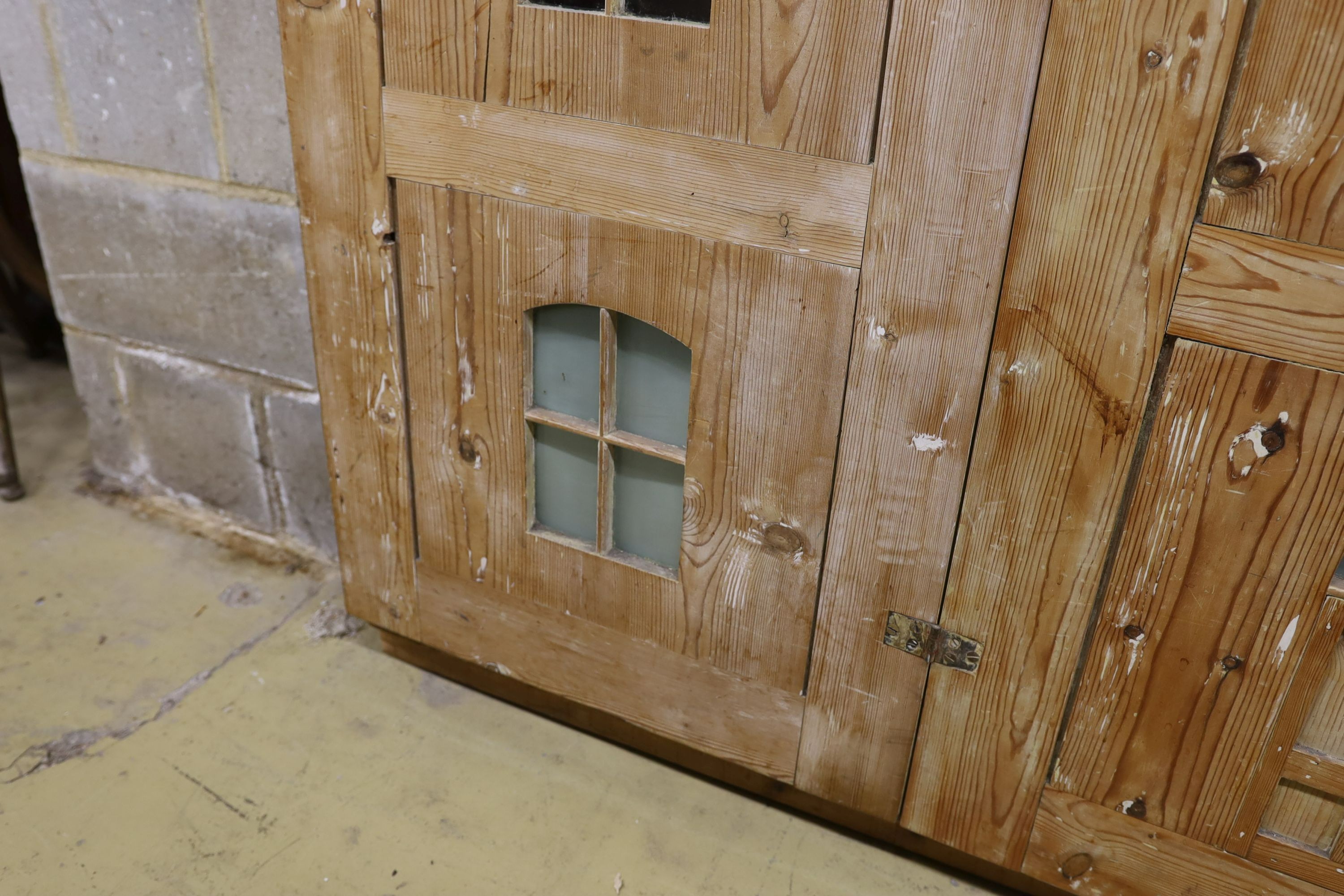 A 19th century stripped pine hall cupboard modelled as a dolls house the two door nine window facade enclosing a compartmented interior, width 182cm, depth 46cm, height 192cm